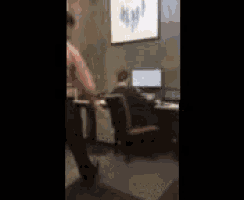 a man is sitting at a desk in front of a computer and talking on a cell phone .