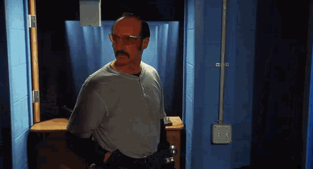 a bald man with glasses and a mustache is standing in a hallway