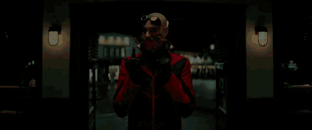 a bald man in a red jacket is walking through a doorway in a dark room