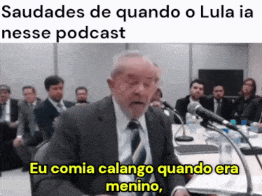 a man in a suit and tie is speaking into a microphone with the words eu comia calango quando era menino below him
