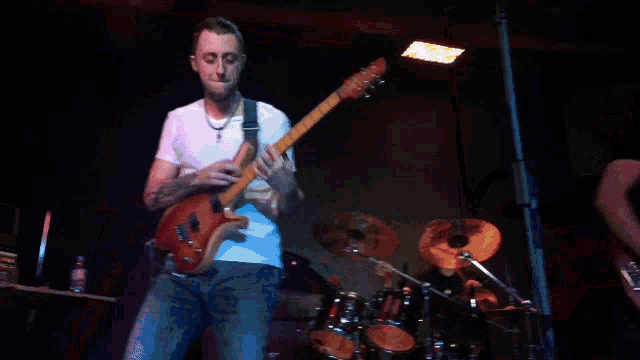 a man playing a guitar on a stage with a drummer in the background