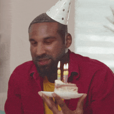 a man wearing a party hat is holding a piece of cake with candles