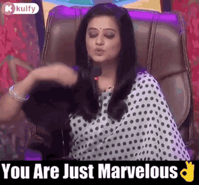 a woman in a polka dot dress is sitting in a chair with a microphone and saying `` you are just marvelous ''
