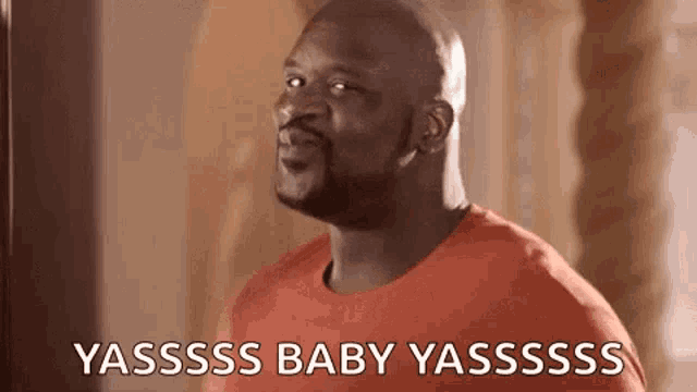 a bald man in a red shirt is making a funny face and saying yassss baby yassss .