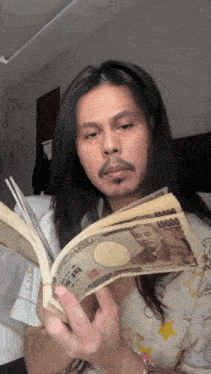 a man with long hair is reading a book while holding a stack of 10000 yen bills