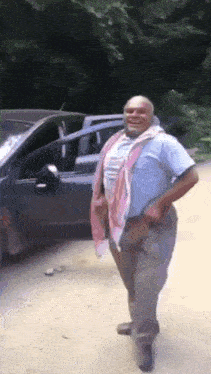 a man in a blue shirt is standing in front of a car .