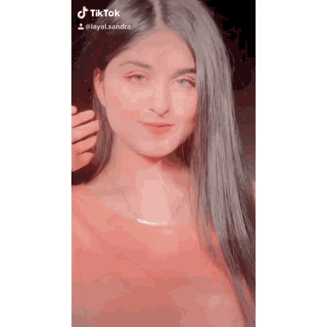 a girl with long black hair is wearing a pink top and a necklace .
