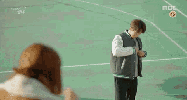 a man is standing on a basketball court wearing a baseball jacket .