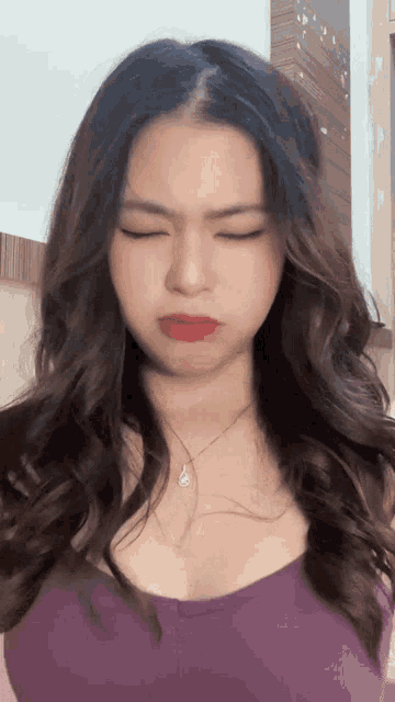a woman wearing a purple top and a necklace is making a funny face
