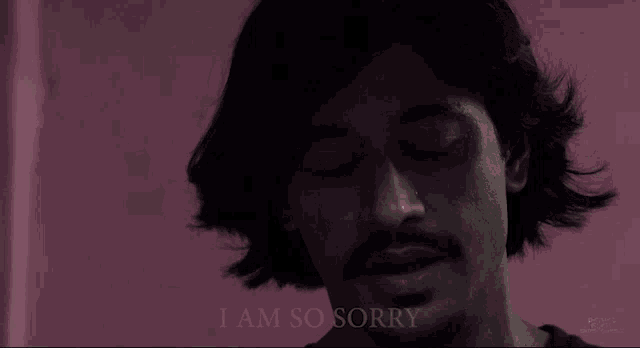 a man with a beard says i am so sorry in front of a pink wall
