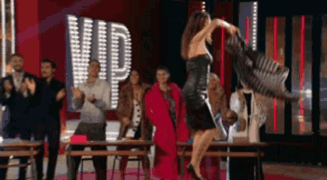 a woman in a black dress is jumping in the air in front of a vip sign