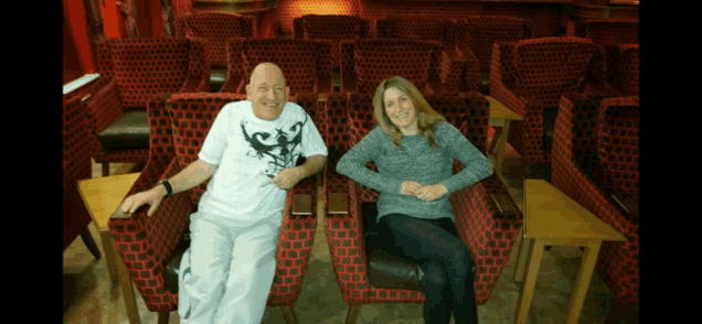 a man and a woman are sitting in red chairs in an empty auditorium