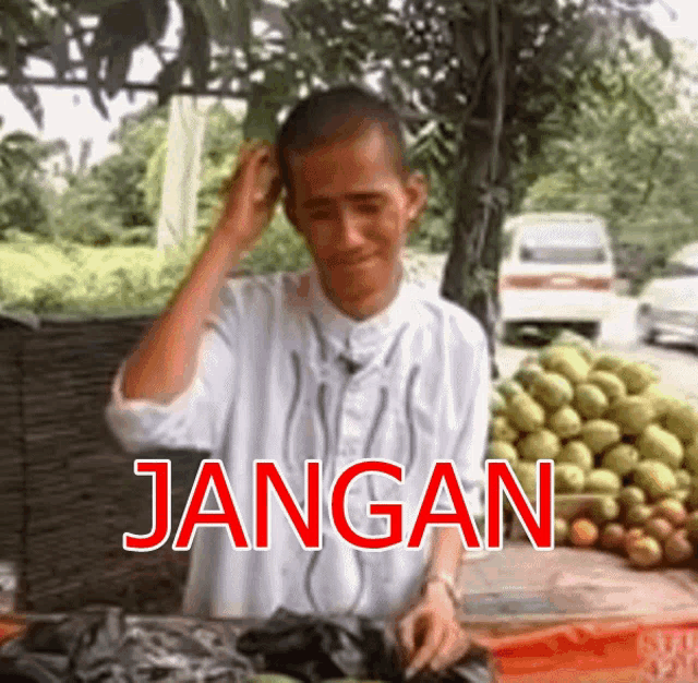 a man is standing in front of a bunch of fruit and the word jangan is written in red