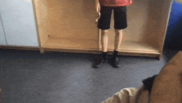 a person wearing black shorts and black shoes stands in front of a wooden shelf