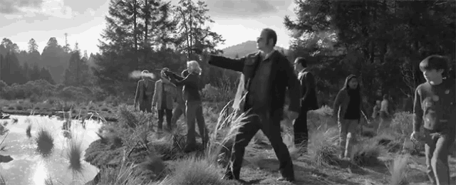 a black and white photo of a group of people standing in a field near a lake .