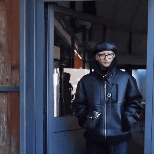 a man wearing glasses and a hat is standing in a doorway .