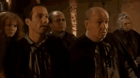 a group of men are standing next to each other in a dark room and looking at something .