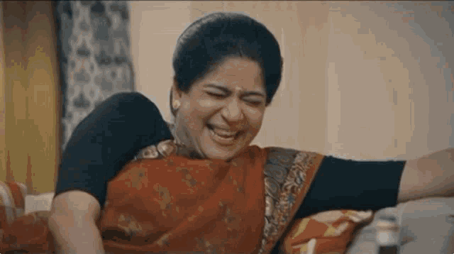 a woman in a red sari is laughing while laying on a bed .