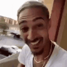a man with a beard is smiling and wearing a white shirt and a gold chain .