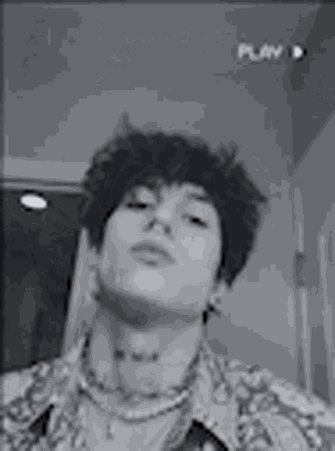 a black and white photo of a young man wearing a necklace and earrings .