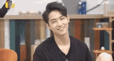 a young man in a black shirt is smiling while sitting in front of a cat tree .