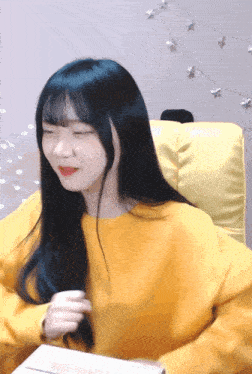 a girl with long black hair is wearing a yellow sweatshirt