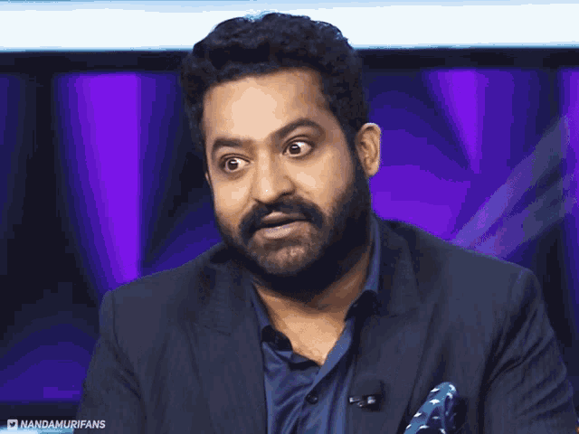 a man with a beard is wearing a suit and a blue shirt with a pocket square that says nandamurifans on it