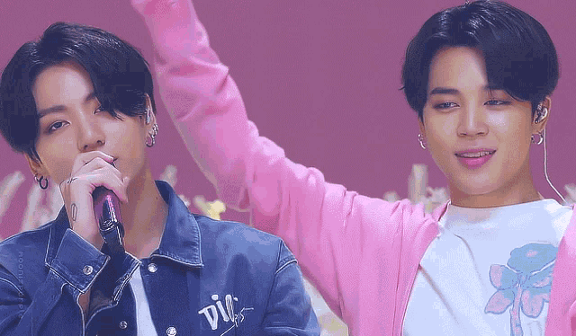 a man wearing a pink cardigan stands next to a man wearing a denim jacket that says " vic " on the back
