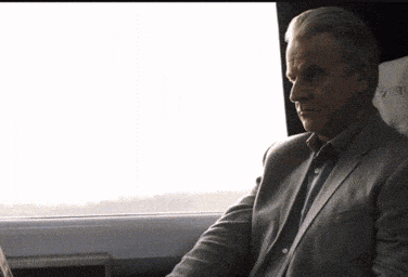 a man in a suit is sitting in a car and looking out the window