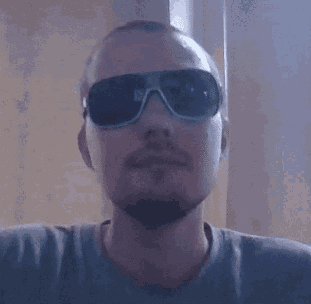 a man with a beard is wearing sunglasses and a grey shirt