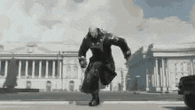 a man in a trench coat is running down a street in front of a large building .
