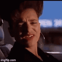 a woman is sitting in a car with her eyes closed and making a funny face .
