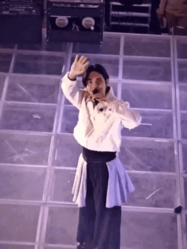 a man stands on a stage holding a microphone and waving his hand