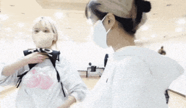 two women wearing masks are standing next to each other .