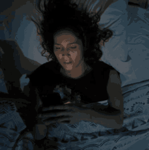 a woman is laying in bed looking at her cell phone