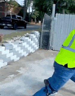 a man wearing a neon yellow safety vest is standing in front of a brick wall .