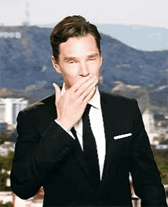 a man in a suit and tie covers his mouth with his hand