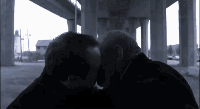 two men are kissing under a bridge in a dark room
