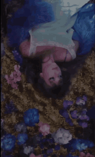 a woman in a blue dress is laying in a bed of flowers .
