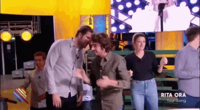 a group of people dancing in front of a screen that says rita ora