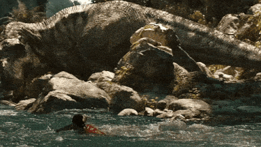 a woman is swimming in a river with a large dinosaur in the background