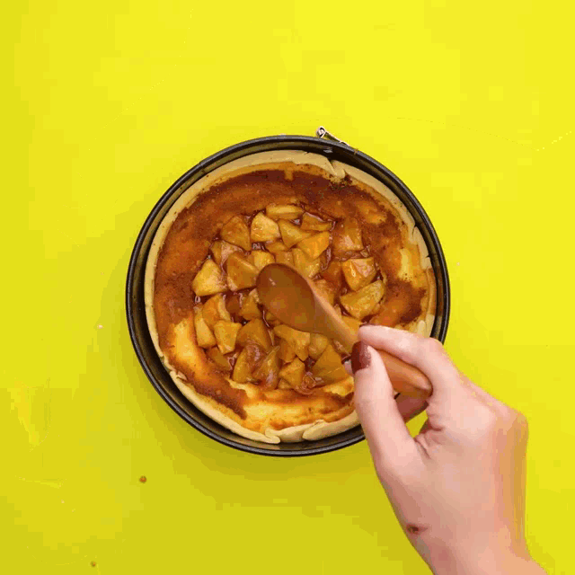 a person is using a wooden spoon to spread caramel on top of an apple pie