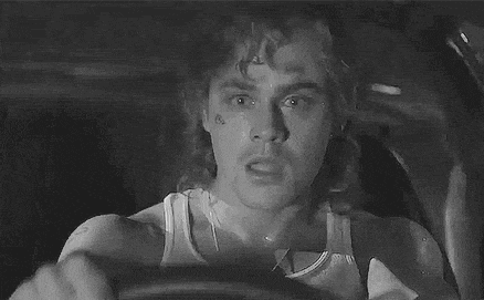 a black and white photo of a man driving a car with a tattoo on his face .