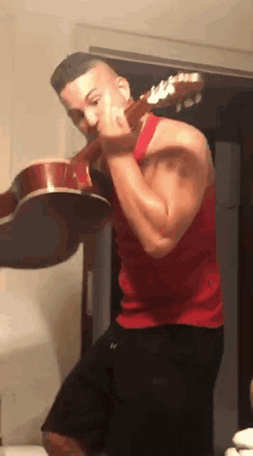 a man in a red tank top is holding a guitar in front of his face