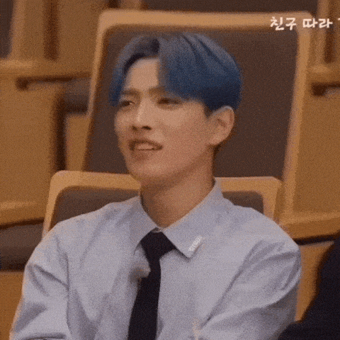 a young man with blue hair is sitting in a chair wearing a blue shirt and a black tie .