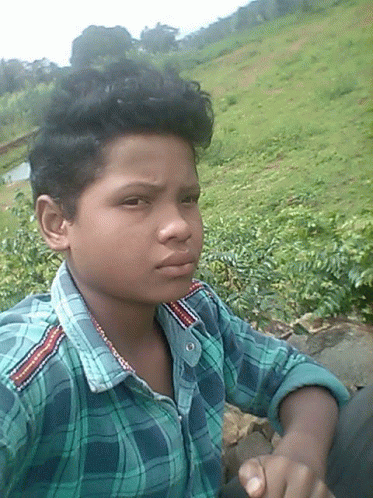 a young boy wearing a plaid shirt is sitting in a field