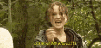a young girl is standing in the woods holding a knife .