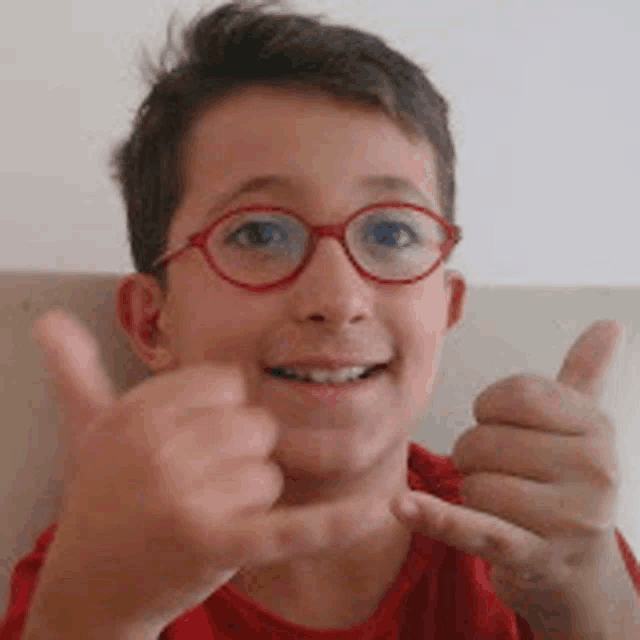 a young boy wearing red glasses is giving a thumbs up