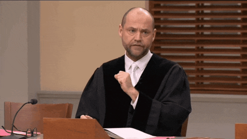 a man in a judge 's robe is sitting at a podium with his fist in the air