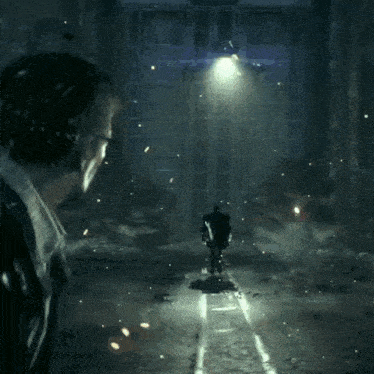 a man in a suit stands in a dark room with a light shining on him